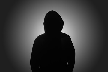 Mysterious man wearing black hoodie standing against dark background. Hacker, crime, and cyber security concept.