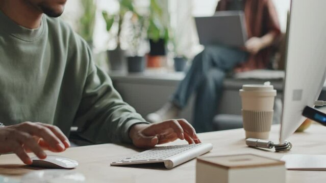 Medium close-up of developer sitting at his workplace with computer and typing on keyboard