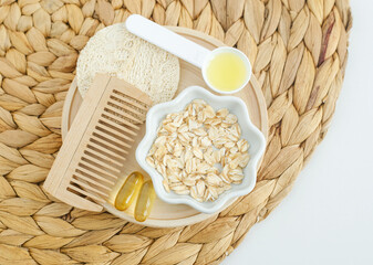 Small bowl with rolled oats, fish oil capsules, olive oil and wooden hairbrush. Ingredients for preparing homemade hair or face mask, natural beauty treatment and spa recipe. Top view, copy space.