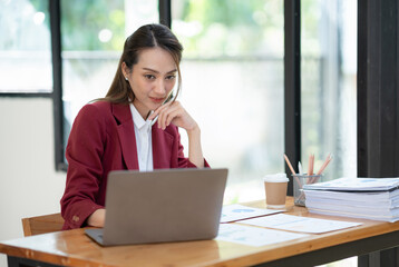 Young Asian businesswoman holding a pen sitting and analyzing the details of management information Finance is happy at the desk in the office. © crizzystudio