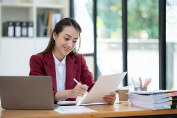 Asian businesswoman sitting happily in office holding detailed report paper analyzing data accuracy in financial matters management concept.