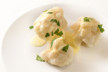 Cooked cauliflower with hollandaise sauce and parsley garnish on a white plate, vegetable side dish, copy space, selected focus