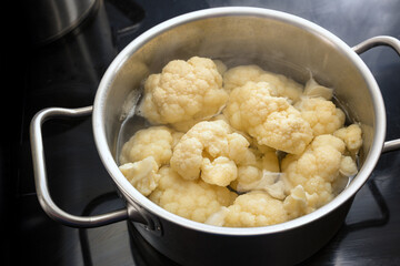 Cooking pieces of cauliflower in boiling water in a stainless steel pot on a black cooktop, healthy...