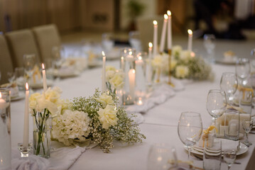 Table setting, serving closeup. Wedding setup detail. Banquet decoration in hall restaurant. Luxury reception. Festive table covered tablecloth, decorated composition flowers and candles in party area