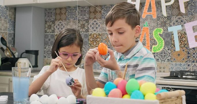 Children painting easter eggs, basket full of colorful easter eggs and happy easter garland background