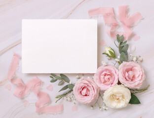 Blank paper card between pink roses and pink silk ribbons on marble top view, wedding mockup