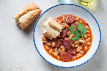 White plate with chorizo and bean stew, elevated view on a light-beige stone background, studio shot