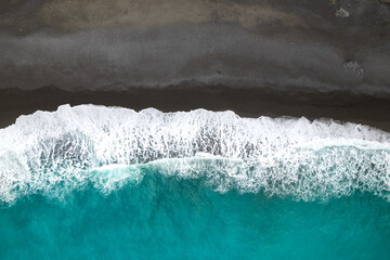 Vue aérienne d'une plage de sable noire et eau turquoise avec des vagues sur l'ile de Majorque...