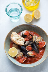 Plate with steamed mussels and littleneck clams served in thick tomato broth, vertical shot on a light-grey granite background