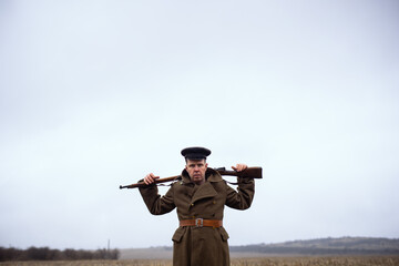 a cool retro soldier of the first world war boldly holds a weapon around his neck and looks evilly...