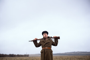 funny comic soldier of the first world war holding a rifle on his neck on his shoulders and looking at the sky. a soldier of the USSR whistles in the field.