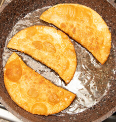 Pasties made from dough and minced meat are fried in oil in a frying pan.
