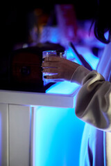 A girl in dim blue light holds a transparent glass with an alcoholic drink in her hands.
 
