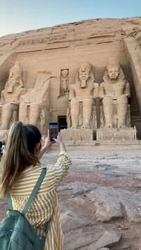 Vertical view of backwards tourist woman taking photos for social media to Abu simbel temple in Egypt