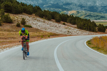 Fototapeta premium Full length portrait of an active triathlete in sportswear and with a protective helmet riding a bicycle. Selective focus 
