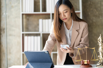 Justice scales and judge hammer on table in lawyer office, Asian woman holding smartphone doing legal work using tablet at lawyer office, online legal consulting concept