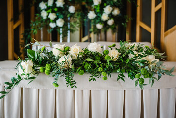 Festive table with tablecloth near arch, decorated with composition of flowers and greenery,...