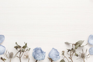 Pretty shabby chic decorative frame with blue roses and dried flowers on a white wooden table	