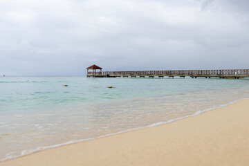 A pier goes into the sea,at the end there is a gazebo.The blue sea water and the sky are separated by the horizon line,a pier.Caribbean Coast in the Dominican Republic.A wave runs over the sandy shore