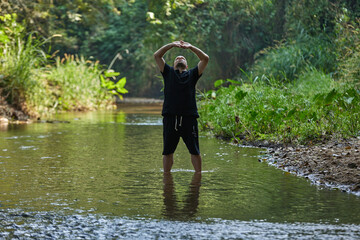 A man practices qigong and taijiquan while standing in a river in the jungle