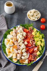 Tradition Cobb salad with fried chicken, avocado, fresh tomatoes, eggs, bacon and cheese on a plate on a dark background. Top view, copy space, selective focus