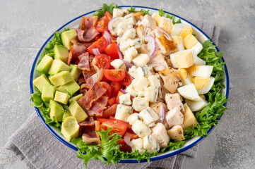 Tradition Cobb salad with fried chicken, avocado, fresh tomatoes, eggs, bacon and cheese on a plate. selective focus