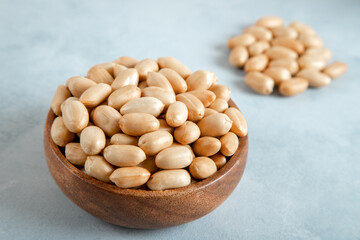 Bowl full of roasted peeled peanuts on bright background