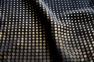 Defocused blurred golden polka dot pattern on black folded fabric as background