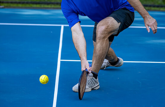 Male pickleball player digs deep to scoop up the ball off the court surface