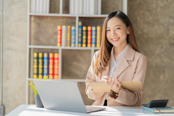 Asian businesswoman holding financial documents to check calculations on laptop or analyzing report...
