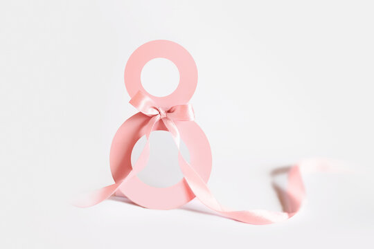 Pink paper cut eight with ribbon on white background. Postcard March 8 concept