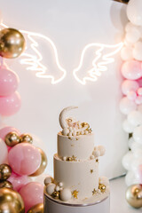 Celebration baptism concept. Arch decorated with pink, white, golden balloons, angel wings. Trendy cake with decor. Reception at birthday baby party on wall. Delicious reception on photo zone, area.
