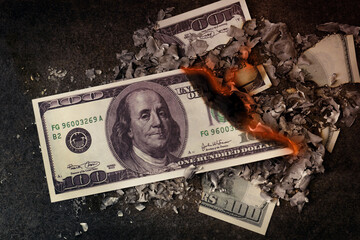 a hundred dollars burn in a fire on a black background, the concept of burning money, inflation, the cost of money,