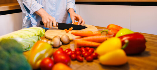 Vegetarian home recipe. Cropped shot of women cooking together, preparing salad. Lady cutting red bell pepper.