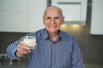 Glass of milk in hand of blurred senior male smiling person