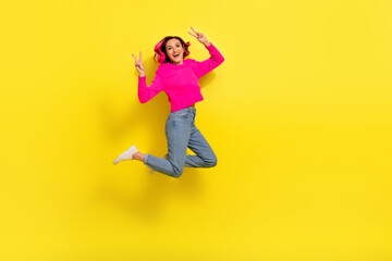 Full length photo of excited friendly lady wear vivid sweater showing v-signs jumping empty space isolated yellow color background