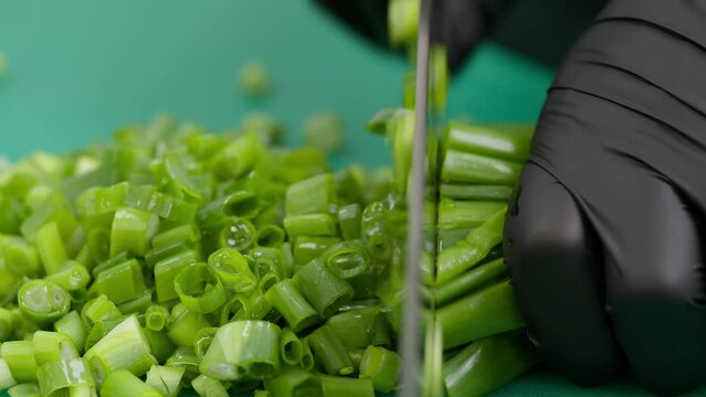 Close-up of a chef's gloved hand quickly slicing celery on a board