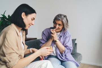 Attentive mother watching adult daughter unwrap present