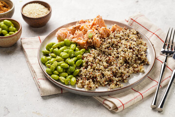 A flat grey plate with quinoa tricolore, roughly chopped and pulled salmon and steamed green soy beans edamame with sesame seeds and deep fried onions on light background