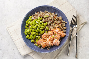 A green bowl with quinoa tricolore, roughly chopped and pulled salmon and teamed green soy beans edamame on light background. Top view