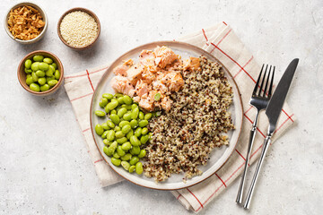 A flat grey plate with quinoa tricolore, roughly chopped and pulled salmon and steamed green soy...