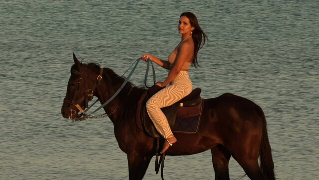 Beautiful elegant young woman riding a black horse, with the sea in the background