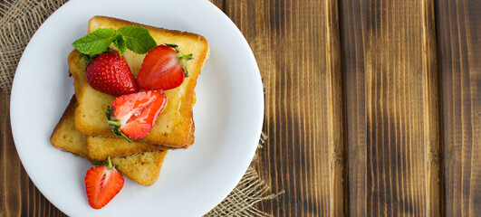 French toasts with strawberries and honey in the white  plate on the rustic wooden background. Top view. Copy space.