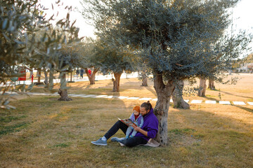 Dad and baby read a book under a tree in the park.