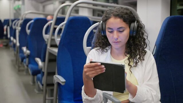 Woman traveler in headphones using digital computer in train