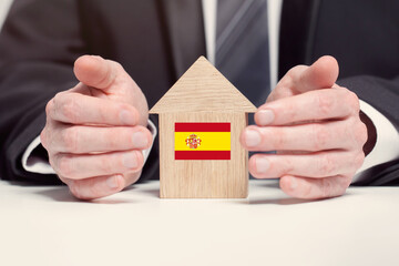 Businessman hand holding wooden home model with Spanish flag. insurance and property concepts