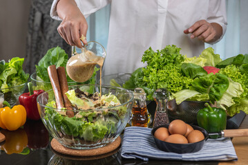 woman chef mix fresh baby cos salad and pour salad dressing in glass blow. Organic Vegetables mix all green salad In glass bowl. Breakfast fresh salad and clean vegetable.