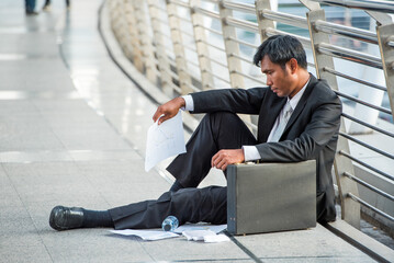 businessman in suit fired from job sitting sad outside office in city background Unemployment, unemployed man with leather briefcase sit on street he loss job. - obrazy, fototapety, plakaty