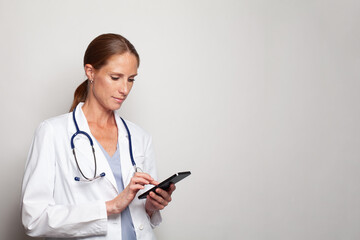 Portrait of confident mid adult woman medical worker or nurse wearing doctor uniform using smartphone, modern female indoor