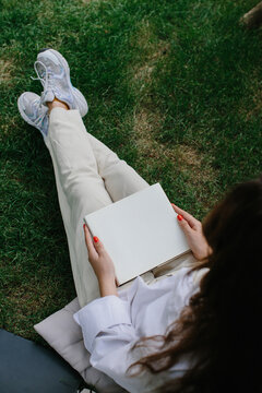 Magazine or book image mockup. The girl relaxes on the lawn in the courtyard of the coffee shop, reads a book.